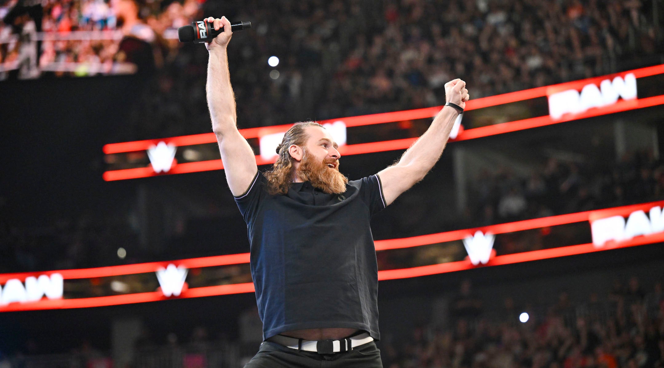 A wrestler gestures in the air holding a microphone